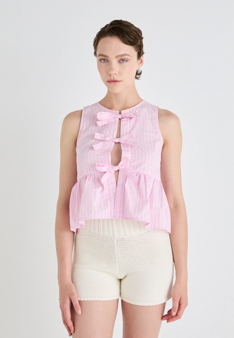 Top senza maniche a righe rosa e bianche con design a peplum, caratterizzato da tre fiocchi decorativi e un'apertura a chiave frontale.