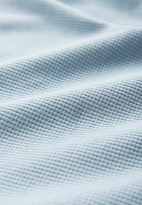 Lyseblåt tekstureret stof med et gittermønster, der har en blød, vævet overflade, som virker let krøllet og lagdelt.