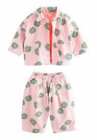 Kortärmad rosa jacka och matchande shorts med gröna blommor och orange mittknappar. Tyget verkar lätt och har en avslappnad passform.