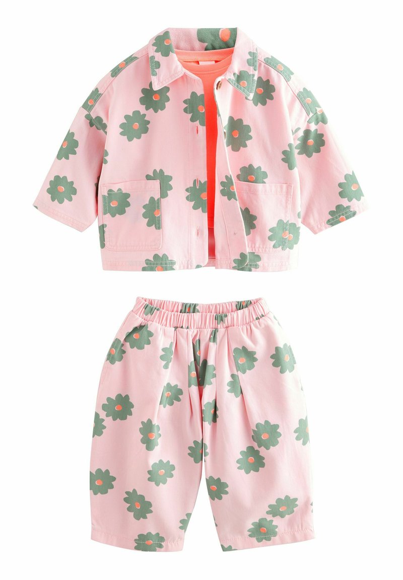 Kortärmad rosa jacka och matchande shorts med gröna blommor och orange mittknappar. Tyget verkar lätt och har en avslappnad passform.