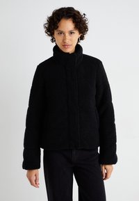 Jachetă din fleece neagră cu guler înalt, suprafață texturată și fermoar frontal. Are mâneci largi și un design croppat.