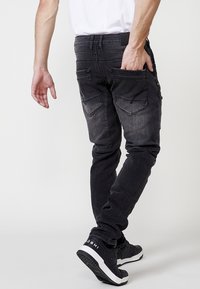 Črne denim hlače slim fit kroja, z bledečo teksturo, več žepi in oznaka na pasu. Oblečene z črnimi supergami.