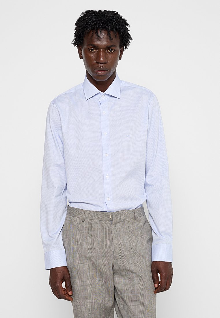 Camisa de manga larga a cuadros azul claro con cuello abotonado. La tela es suave con cuadros sutiles, combinada con pantalones de cuadros gris.