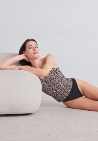 Leopardenmuster-Trägershirt mit dünnen Trägern, kombiniert mit schwarzen hoch geschnittenen Panties, auf einem strukturierten weißen modernen Sofa in einem neutralen Farbschema.