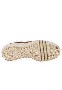 Zapatilla marrón con una suela de goma beige texturizada que presenta un patrón hexagonal, detalles de marcaje y tres ranuras distintas para mayor flexibilidad.