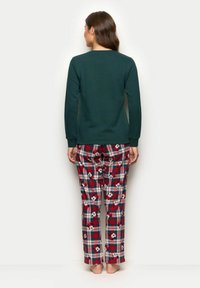 Zelený top s dlouhým rukávem spojený s kostkovanými pyžamovými kalhotami v červeném, černém a bílém kostkovaném vzoru, doplněnými potisky s postavičkami z kreslených filmů.