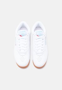 Ζευγάρι λευκά sneakers Reebok με λεπτομέρειες λογότυπου σε ανοιχτό μπλε και κόκκινο, λευκά κορδόνια και σόλες από καουτσούκ χρώματος καραμέλας, απεικονισμένα από πάνω σε απλό φόντο.