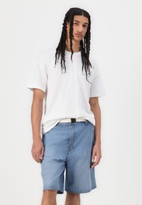 Hvit bomulls t-skjorte med korte ermer, kombinert med lyseblå denimshorts. Shortsene har en sidesøm og et enkelt hvitt belte.
