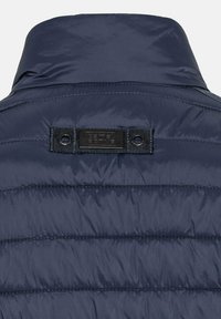 Navy pufferjackets met een genaaid textuur, voorzien van een zwart label met branding, twee drukknoopsluitingen en versterkte stikdetails.