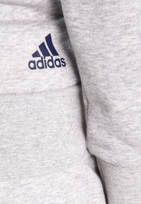 Sweat-shirt en coton gris clair avec un logo Adidas bleu marine. Le tissu a une texture douce avec une finition lisse et des poignets côtelés.
