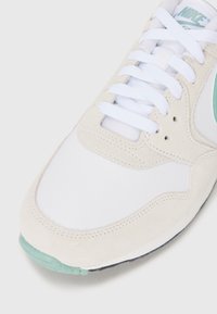 Białe sneakersy zamszowe i siateczkowe, z miętowym akcentem, okrągłym noskiem i białymi sznurówkami. Jasna, neutralna kolorystyka.