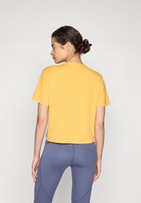 T-shirt jaune à manches courtes avec un col rond et une coupe décontractée, associé à des leggings gris ajustés affichant des détails de couture.