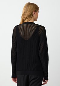 Maglione nero lavorato a maglia con un design aperto e strutturato. Presenta maniche lunghe, un retro a forma di V e orli a coste. Materiale morbido e leggero.