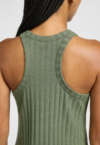 Top a canottiera a coste color verde oliva con design racerback. Presenta un tessuto testurizzato e un piccolo logo sul colletto.