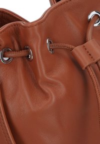 Braune Leder-Eimer-Tasche mit silbernen Beschlägen, ausgestattet mit einem Kordelzugverschluss und einer weichen, strukturierten Oberfläche.