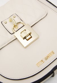 Krémová kožená kabelka s diamantovým prošíváním, zlaté kování, černé švy a embosované logo "Steve Madden".