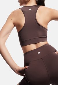 Brun trænings crop top og høj talje leggings, lavet af strækbart materiale. Har et logo på bagsiden og hoften, sømløs design.