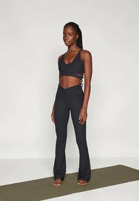 Fekete sportos öltözet, amely crop toppal rendelkezik, kivágott részletekkel és magas derekú, bővülő leggings-szel. Puha, rugalmas anyag.