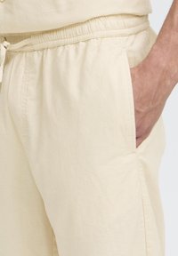 Pantaloni di cotone beige chiaro con vita elastica e coulisse, dotati di tasche laterali e vestibilità comoda e rilassata.