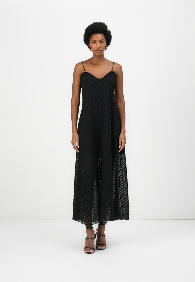 Black maxi dress with thin straps, featuring a textured open weave pattern, V-neckline, and flowy silhouette. Shoes are black strappy sandals.