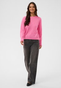 Un pull rose clair en texture douce, à encolure ronde, assorti à un jean large gris foncé et des ballerines noires. Design minimal sans accents.