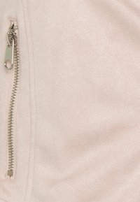 Giacca rosa chiaro con una consistenza morbida, caratterizzata da una zip laterale in metallo argento. Il tessuto liscio e una leggera lucentezza sono evidenti.