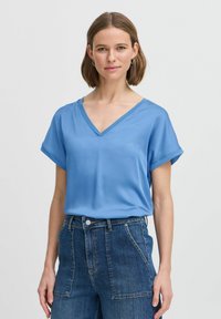 Heled sinise lühikeste varrukatega blouse, millel on V-dekoltee, valmistatud siledast kangast. Koos kõrge vöökohtaga siniste denimipükstega, millel on taskud.
