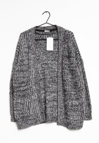 Grå stickad cardigan som hänger från en svart krok, med lös passform, öppen front och en tagg fäst vid kragen.