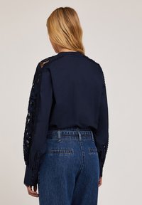 Marinblus med intrikata spetsdetaljer på ärmarna, textil med struktur, långa ärmar och knäppning vid ärmsluten, kombinerad med hög midja jeans i denim.