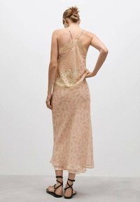 Rochie maxi florală în piersică deschisă, cu dantelă și bretele subțiri. Material moale și semi-transparent, cu o siluetă fluidă și tiv ondulat.