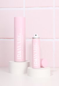 Rosa Aerosol-Haarspray-Dosen mit weißem Text, eine hoch und zylindrisch, die andere kürzer mit einer runden Kappe, auf geometrischen weißen Säulen platziert.