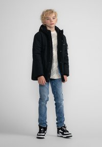 Svart puffjacka med huva, kombinerad med en mönstrad vit tröja och ljusblå jeans. Svart och vita klumpiga sneakers fulländar stilen.