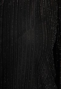 Tessuto nero con strisce verticali argentate scintillanti, che mostra una texture di materiale lavorato a maglia o tessuto, con un leggero effetto lucente.