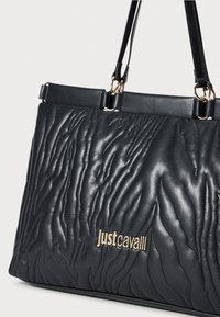 Black quilted leather tote bag with a wave pattern, featuring a gold logo and elegant dual handles for carrying.