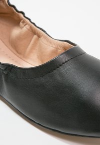 Ballerines noires en cuir avec une finition lisse, bord élastiqué et doublure intérieure beige. Détails de couture subtils près du haut.