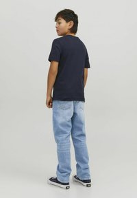 T-shirt en coton bleu marine associé à un jean en denim bleu clair et des baskets noires, vu de dos. Design simple avec des manches courtes et une coupe droite.