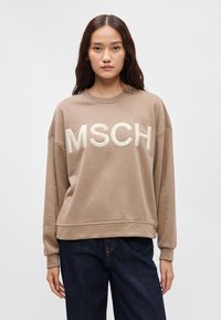 Καφέ φούτερ με την επιγραφή "MSCH" σε ανάγλυφα, ανοιχτόχρωμα γράμματα, με χαλαρή εφαρμογή, λαιμόκοψη και ριμπ μανσέτες. Συνδυάζεται με σκούρα τζιν.