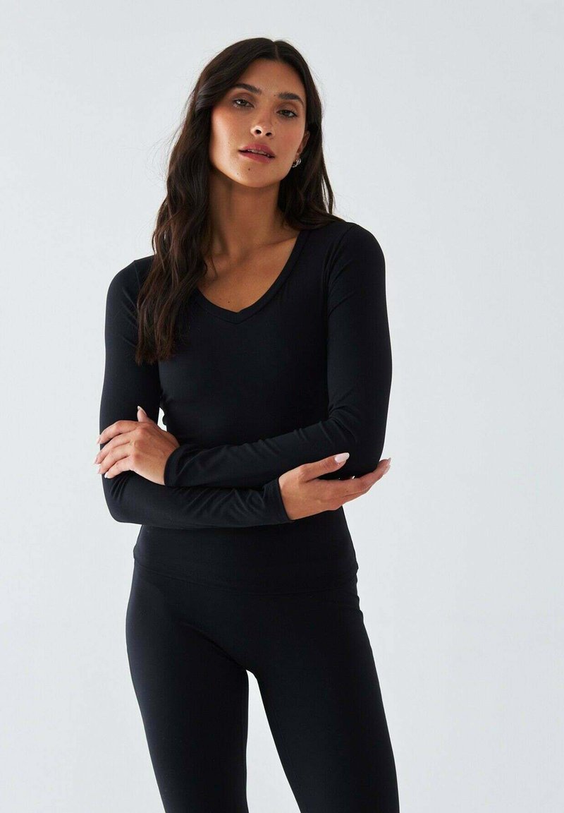 Schwarzes Langarmoberteil mit V-Ausschnitt, gefertigt aus weichem, dehnbarem Stoff. Kombiniert mit passenden schwarzen Leggings, beide figurbetont.