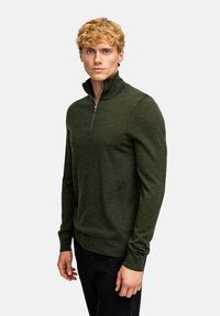 Tussengewicht, donkergroen pullove met een ritssluiting in de kraag, geribde manchetten en een slim fit silhouet. Gemaakt van zacht gebreide stof.