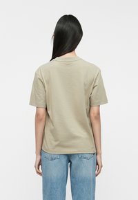Tricou kaki cu mânecă scurtă, fabricat din bumbac moale, cu guler rotund și croială lejere, asortat cu blugi din denim albaștri deschiși.