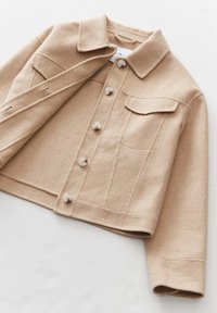 Beige wollen jas met knoopsluiting aan de voorkant, twee klepzakken en een kraag. Heeft een gestructureerd ontwerp en een cropped silhouet.