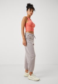 Lys rosa, tettsittende crop tank topp paret med grå joggebukser med elastisk liv og avsluttede anklerr. Modellen har på seg off-white joggesko.