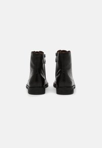 Botines de piel negra con una textura suave, que cuentan con un cierre lateral y un tacón bajo apilado, mostrando un diseño minimalista.