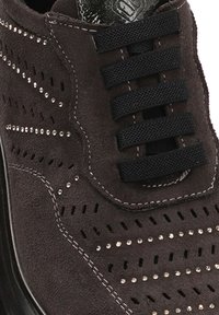 Zapatillas de ante en gris oscuro con cordones negros, que cuentan con perforaciones y adornos de pedrería a lo largo de los lados y una suela de goma.
