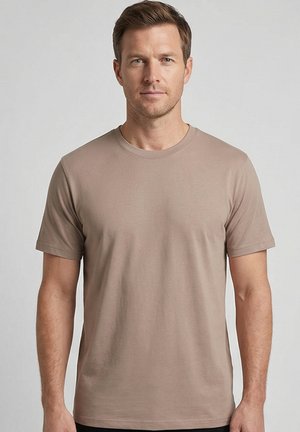 Homme debout, de face, portant un t-shirt uni beige à manches courtes et col rond, sur un fond neutre.
