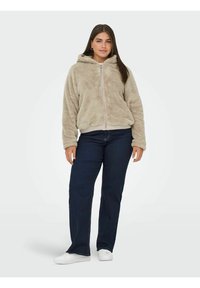 Beżowy polarowy hoodie na zamek z kapturem, charakteryzujący się miękką teksturą i elastycznymi mankietami, w połączeniu z ciemnoniebieskimi dżinsami prostymi i białymi trampkami.