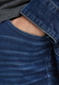 Mörkblå denimjeans med en lätt blekt textur, utrustade med en framficka och en synlig söm. Tyget är tjockt och slitstarkt.