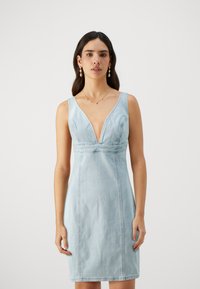 Lys blå denimkjole med dyp V-hals, ermeløs design, tettsittende silhuett og synlige sømdetaljer.