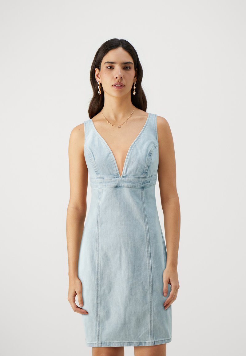 Lys blå denimkjole med dyp V-hals, ermeløs design, tettsittende silhuett og synlige sømdetaljer.