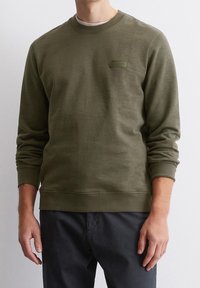 Oliwkowa bluza wykonana z miękkiego materiału, z okrągłym dekoltem, ściągaczami na rękawach i małą naszywką z logo na piersi.